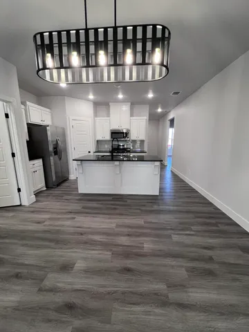 a view of a living room kitchen with stainless steel appliances wooden floor and a chandelier