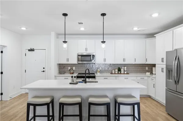 a kitchen with stainless steel appliances granite countertop a sink a stove a refrigerator and white cabinets with wooden floor