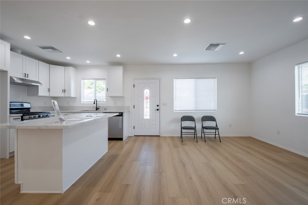 12974 Goleta Street Pacoima, CA 91331 - Photo 5 of 18 a kitchen with stainless steel appliances granite countertop a stove a sink a refrigerator and white cabinets with wooden floor