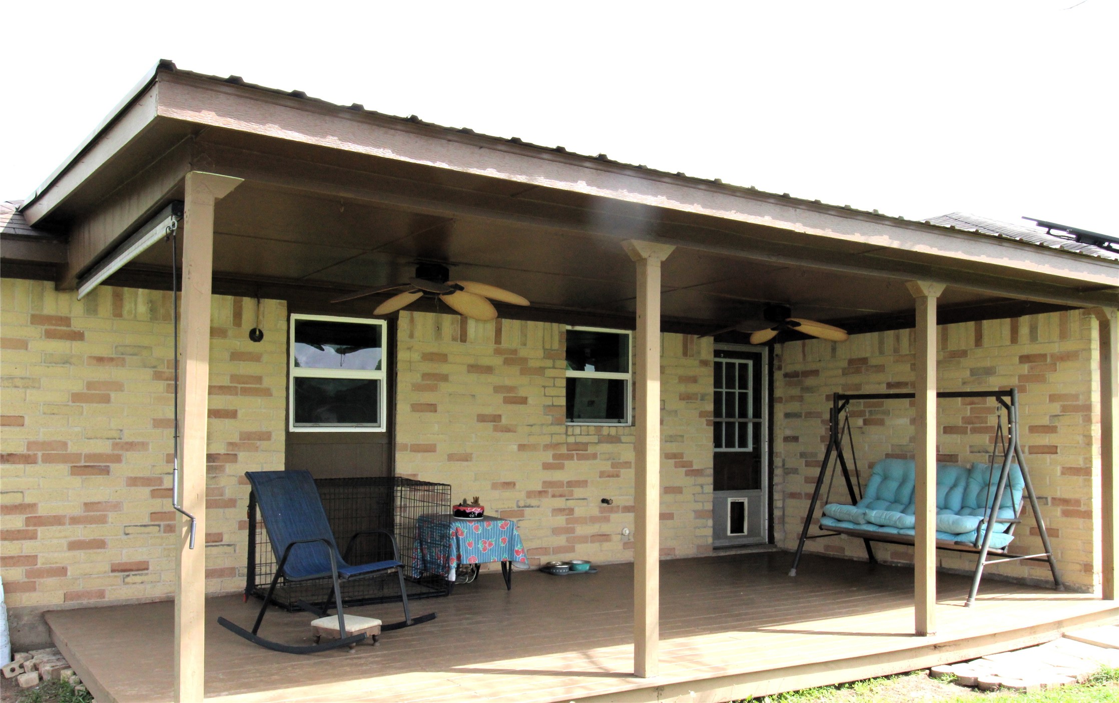 303 North 9th Street Beasley, TX 77417 - Photo 18 of 41 This photo features a covered patio with ceiling fans, a swing bench, and a rocking chair. It offers a cozy outdoor space for relaxation and grilling.
