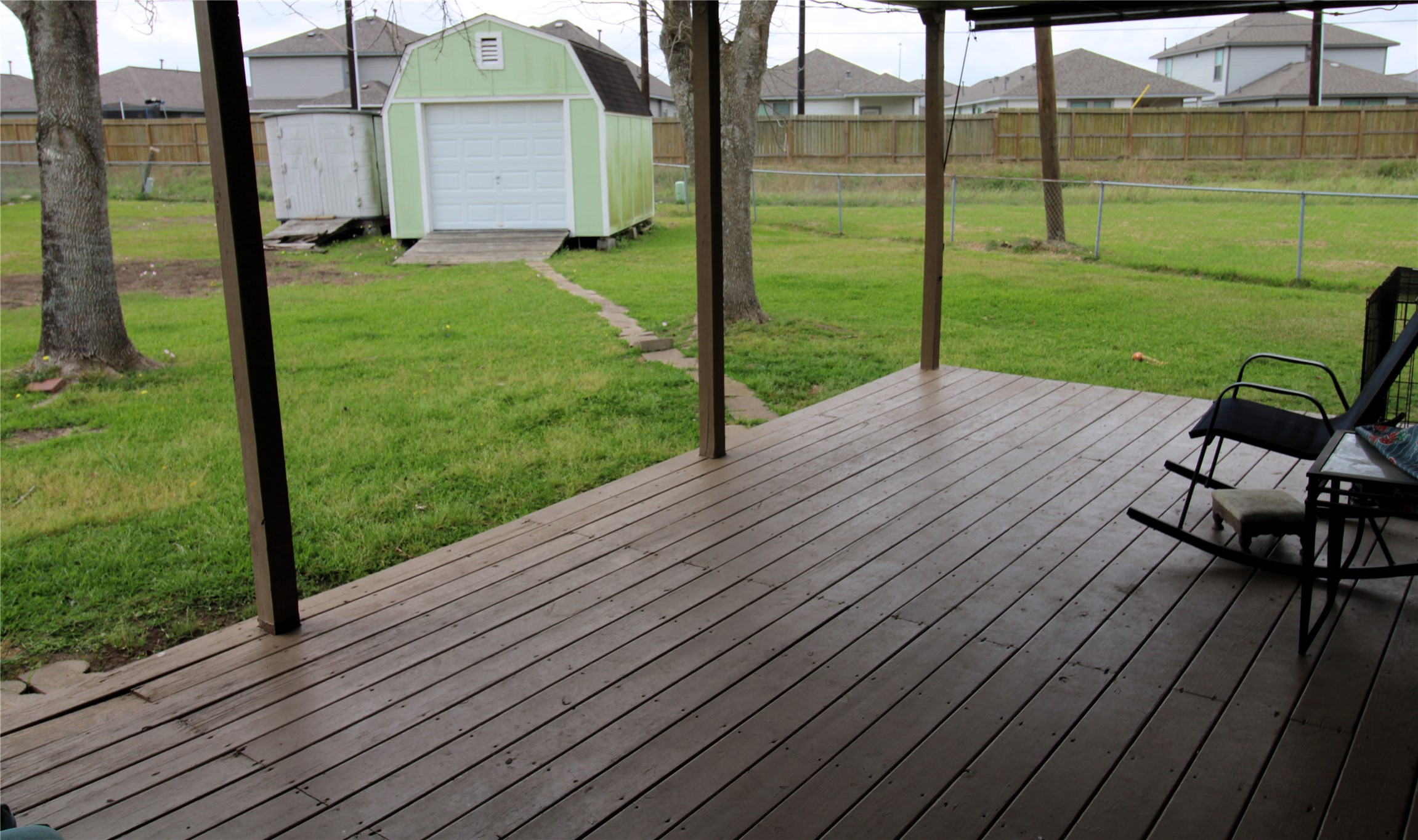 303 North 9th Street Beasley, TX 77417 - Photo 19 of 41 Spacious backyard featuring a covered wooden deck, perfect for relaxing or entertaining. It includes a storage shed and is surrounded by a fenced-in grassy area.