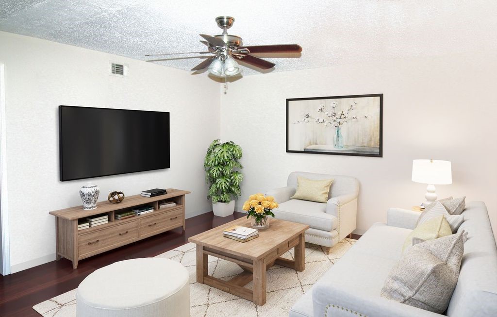 303 North 9th Street Beasley, TX 77417 - Photo 2 of 41 This cozy living room features a modern setup with a large wall-mounted TV, neutral-toned furniture, and a ceiling fan. The space is accented with a potted plant, a decorative vase, and a framed artwork, creating a welcoming atmosphere.