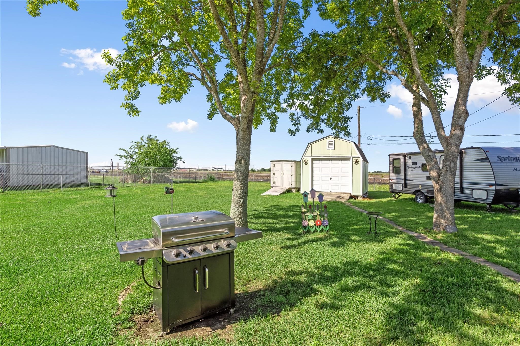 303 North 9th Street Beasley, TX 77417 - Photo 23 of 41 Spacious backyard with lush green grass, featuring trees for shade, a barbecue grill, and two storage sheds. Ideal for outdoor activities and relaxation.