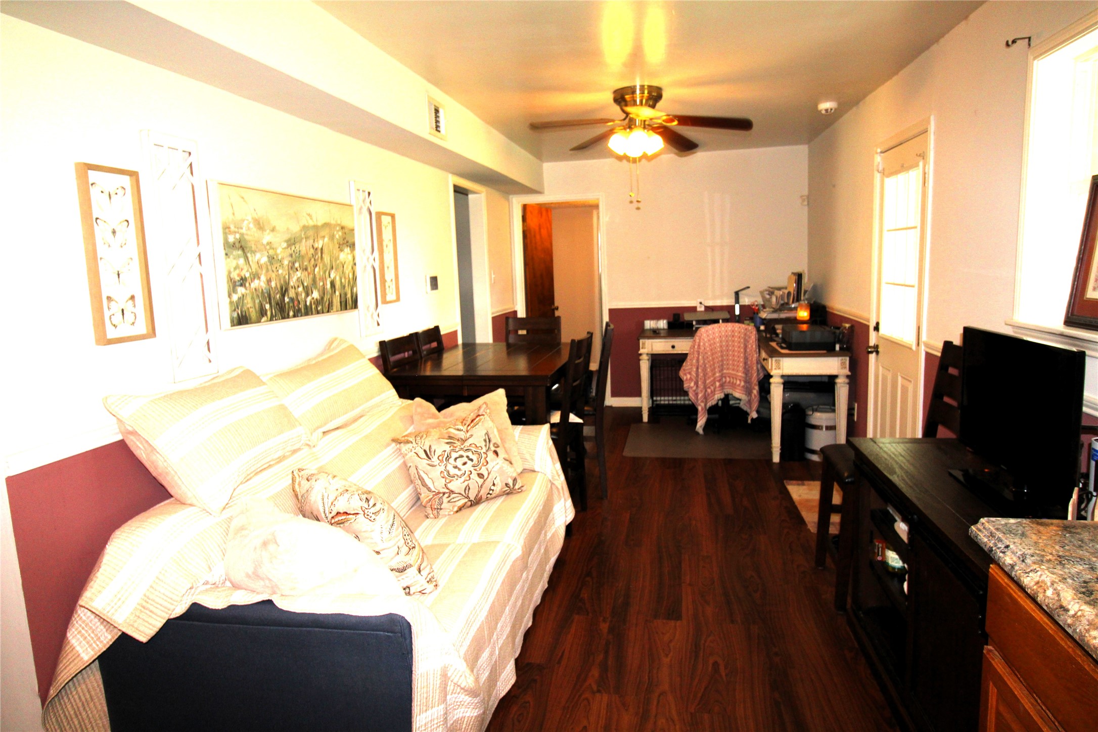 303 North 9th Street Beasley, TX 77417 - Photo 6 of 41 This cozy dining living area features warm wood flooring, a comfortable couch, and a ceiling fan for added comfort. The space is well-lit with natural light from the window, and a small dining area is positioned alongside a functional kitchen setup. Hardwood flooring and practical furnishings make this a welcoming, versatile space.