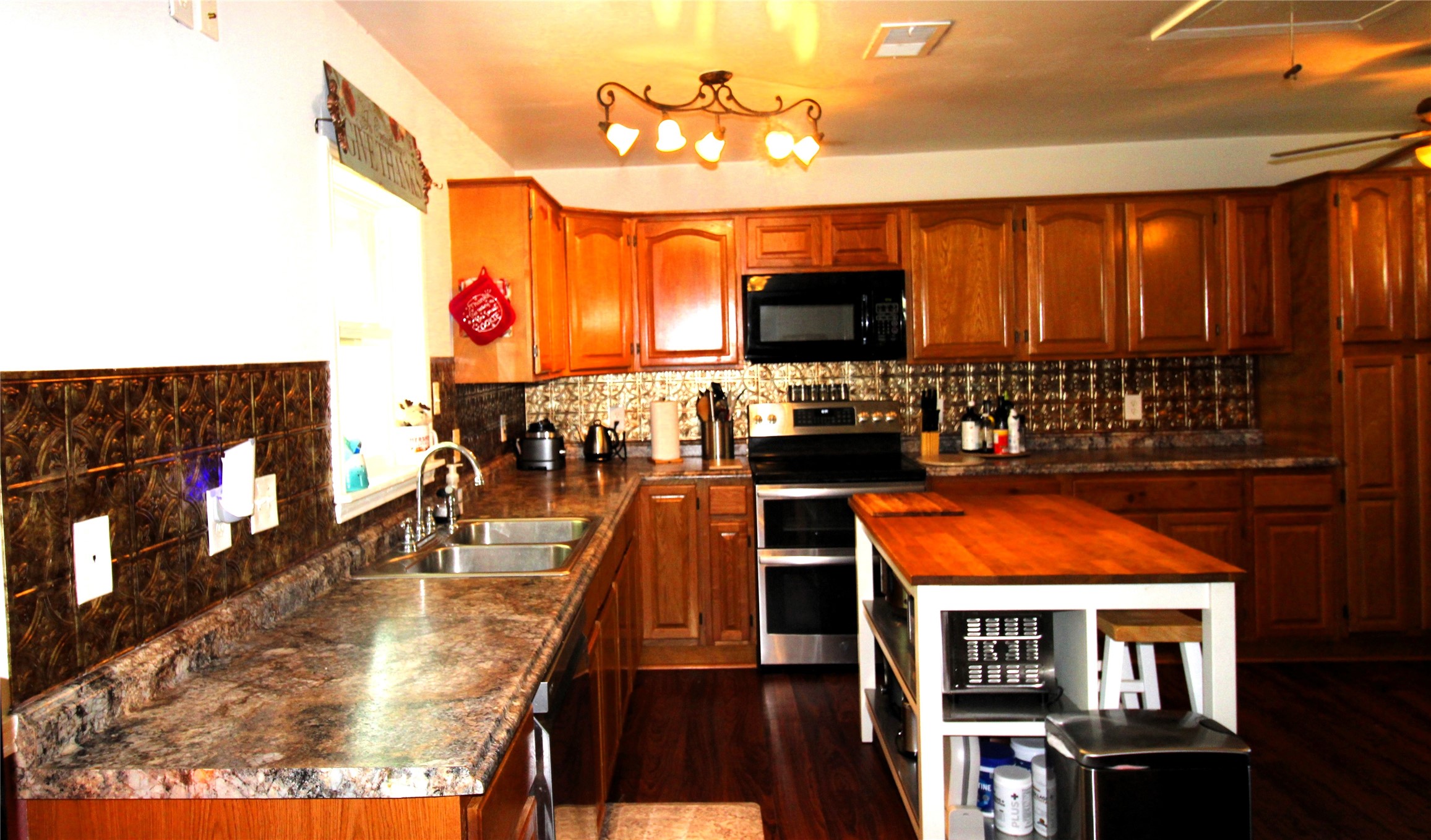 303 North 9th Street Beasley, TX 77417 - Photo 7 of 41 Spacious kitchen with warm wooden cabinetry and modern appliances. Features an island with a wooden countertop and ample storage. The room is well-lit with stylish fixtures, and the copper backsplash adds a touch of elegance.