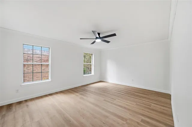 an empty room with wooden floor fan and windows