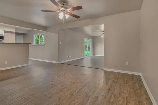 an empty room with wooden floor chandelier fan and windows