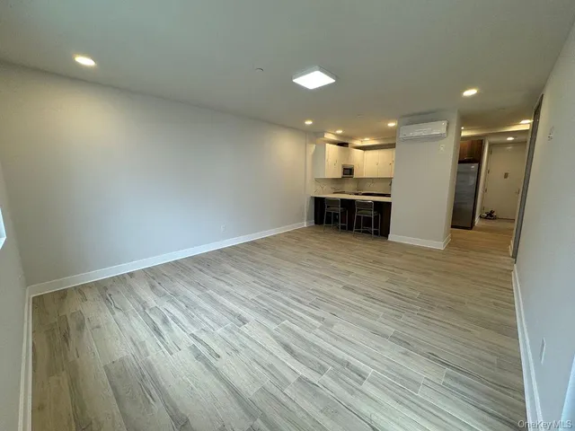 an empty room with wooden floor and kitchen view