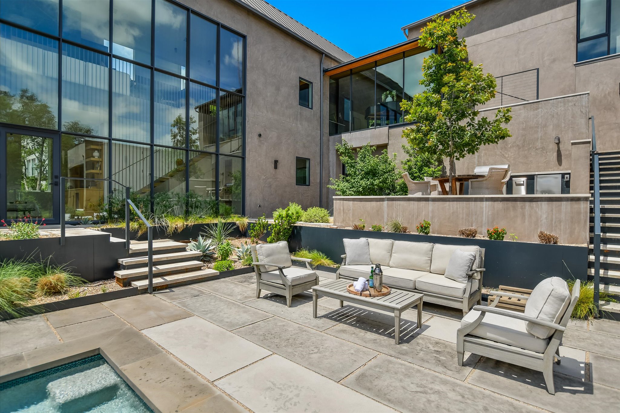 2405 Deer Pass Austin, TX 78746 - Photo 30 of 38 Rear exterior showcasing a large floor-to-ceiling window wall, a tiered patio with stone pavers, built-in outdoor kitchen, and a private spa with tiled interior