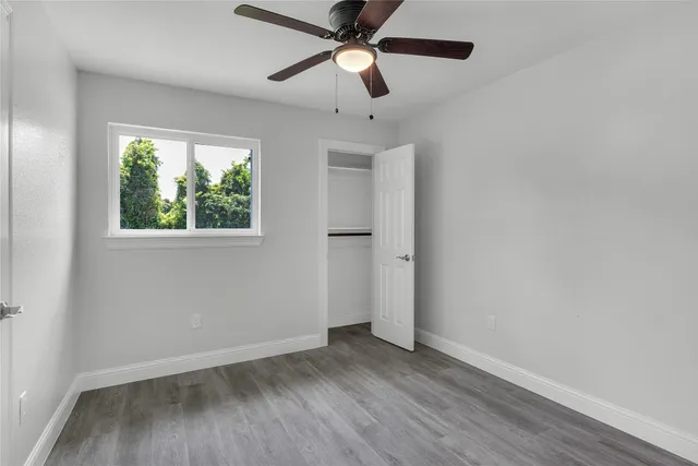 an empty room with wooden floor ceiling fan and windows