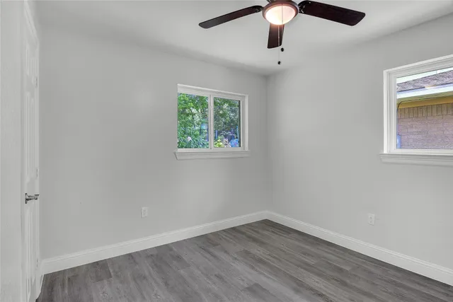 an empty room with wooden floor chandelier fan and windows