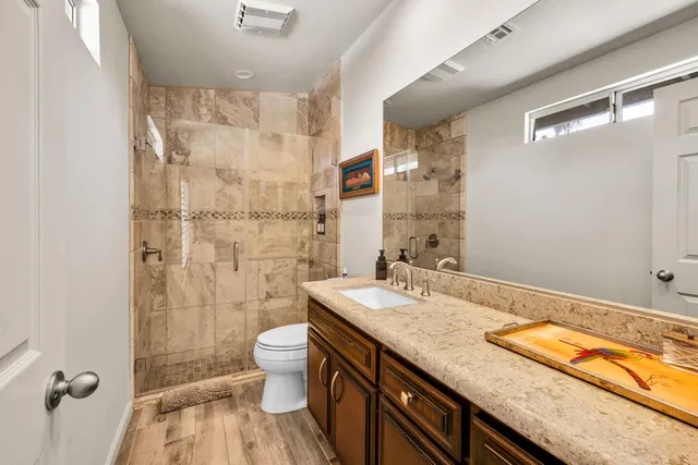 a bathroom with a granite countertop sink a toilet a mirror and shower