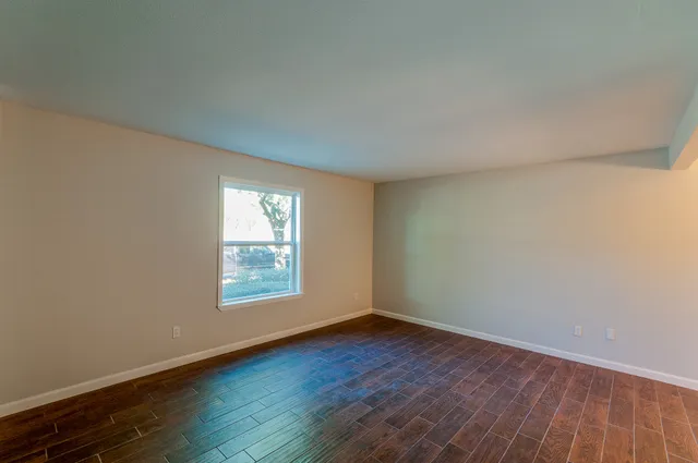 a view of an empty room with wooden floor and a window