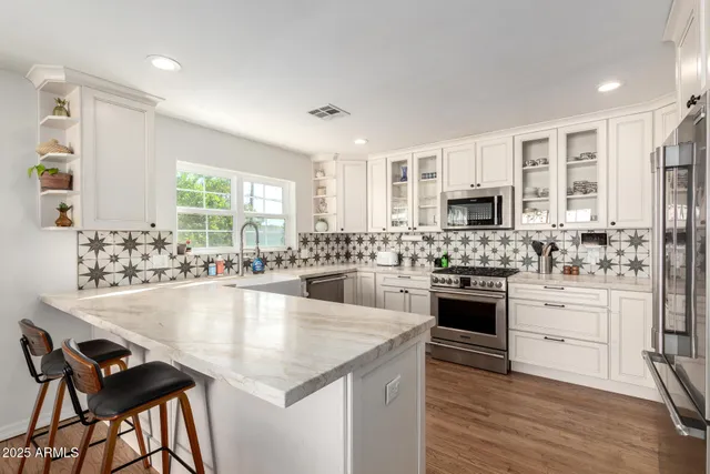 a large white kitchen with granite countertop a stove top oven a sink dishwasher a dining table and chairs with wooden floor