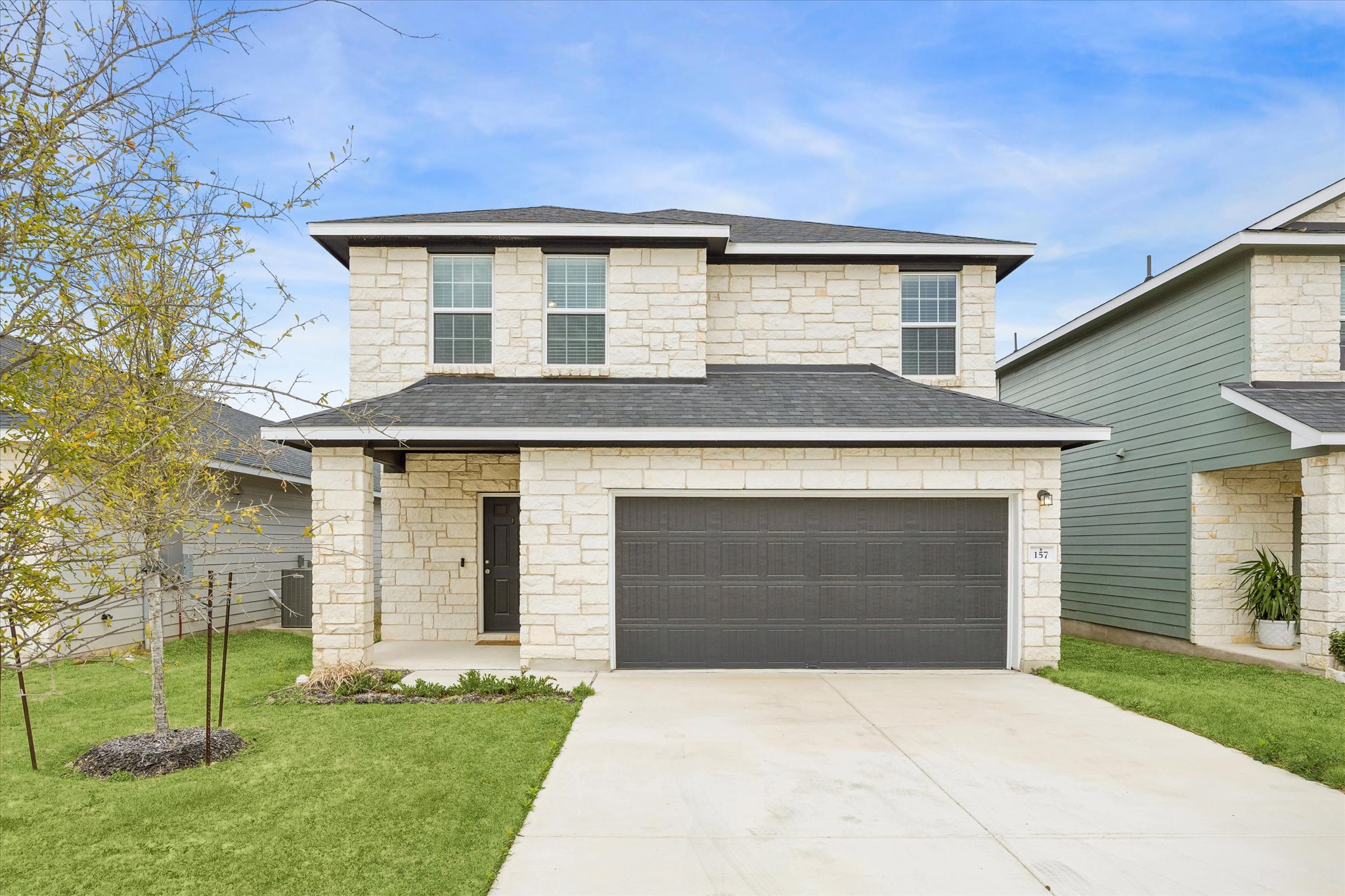 View of front facade featuring stone siding, a front lawn, driveway, and a shingled roof