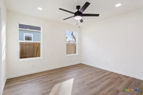 an empty room with wooden floor ceiling fan and windows