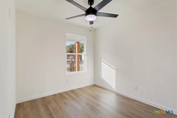 an empty room with wooden floor chandelier fan and windows