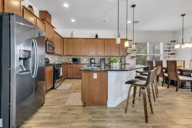 a kitchen with stainless steel appliances granite countertop a refrigerator a sink dishwasher a stove and a dining table with wooden floor