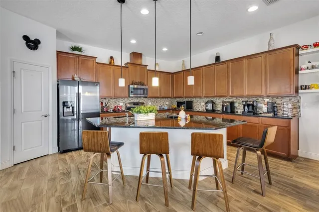 a kitchen with stainless steel appliances kitchen island granite countertop a refrigerator a stove a sink a dining table and chairs with wooden floor