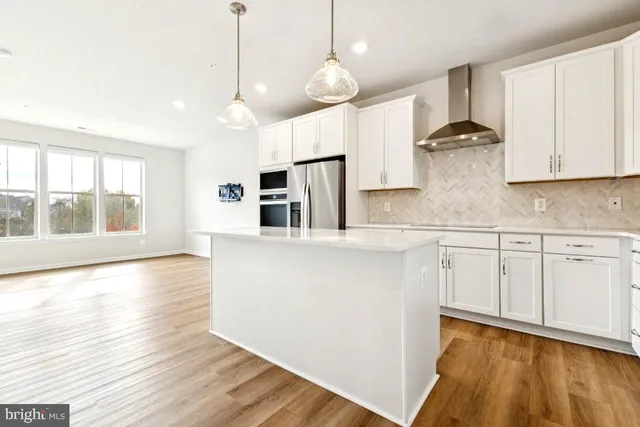 a kitchen with stainless steel appliances granite countertop a refrigerator a sink dishwasher a stove and white countertops with wooden floor