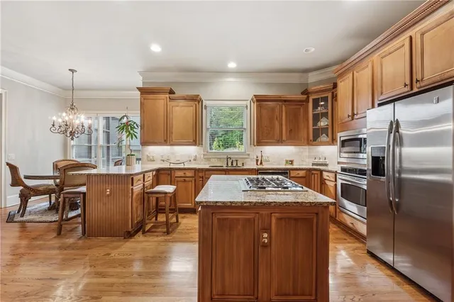 a kitchen with stainless steel appliances granite countertop wooden cabinets a sink a stove a dining table and chairs