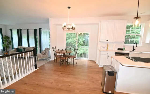 a open kitchen with stainless steel appliances granite countertop a stove top oven a sink a dining table and chairs with wooden floor