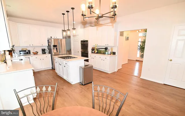 a kitchen with stainless steel appliances kitchen island granite countertop a refrigerator a stove and white cabinets with wooden floor