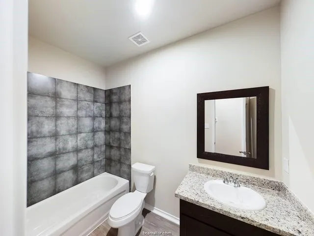 a bathroom with a granite countertop sink a toilet a mirror and shower