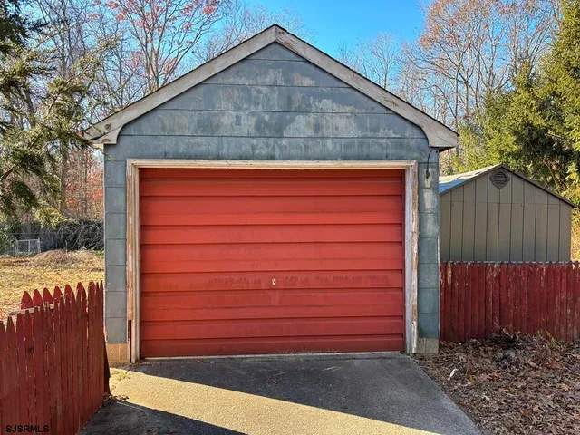 a small barn in front of a house with a wooden fence