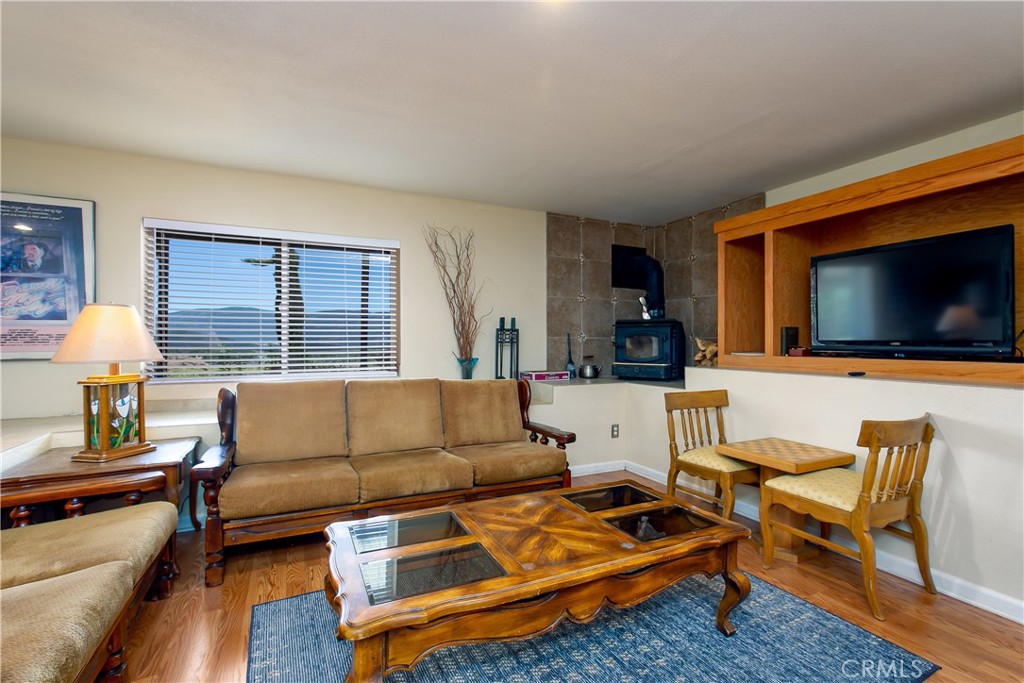 10960 Steinhoff Road Frazier Park, CA 93225 - Photo 36 of 46 Another perspective of the spacious downstairs living room. This view showcases the rich wood flooring, a cozy leather sofa setup, a rustic wood-burning stove framed by a floor-to-ceiling stone accent wall, and a large custom oak built-in entertainment unit with integrated shelving and media space.