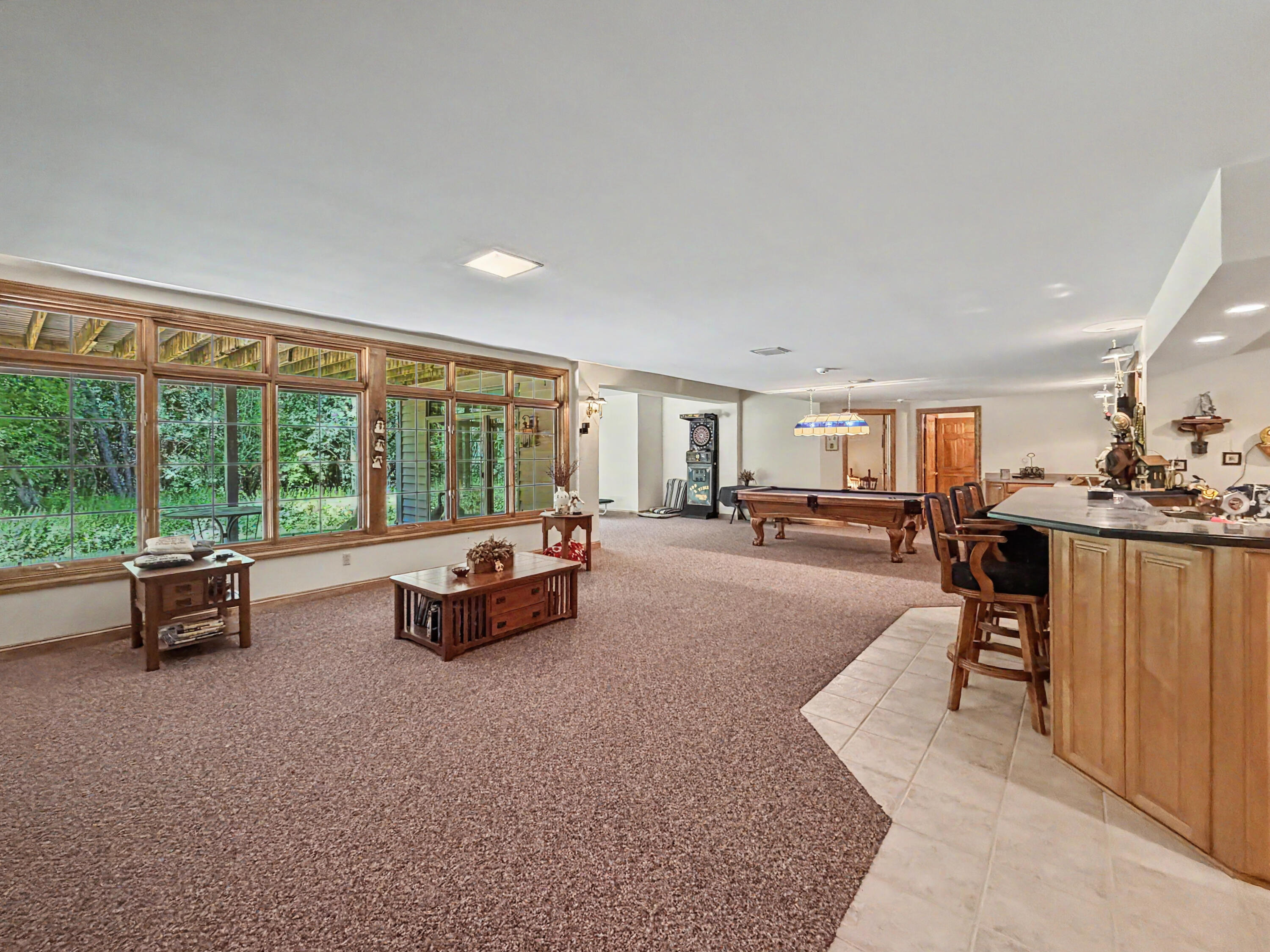 W291-s5245 Ridgefield Road Waukesha, WI 53189 - Photo 31 of 44 The fully exposed walkout lower level is designed for entertaining, featuring expansive recreation space, walls of windows, a custom wet bar with cabinetry and seating, game area, sun-filled sitting room, and direct access to the covered stamped-concrete patio. Surrounded by mature trees and a private wooded backdrop