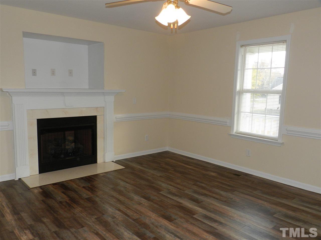 453 Axum Road Willow Spring, NC 27592 - Photo 4 of 17 an empty room with wooden floor fireplace and window