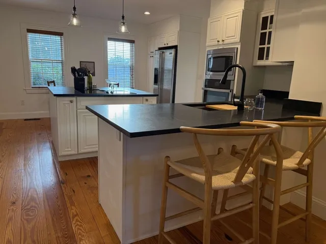 a kitchen with stainless steel appliances granite countertop a refrigerator a sink dishwasher a oven and a dining table with wooden floor