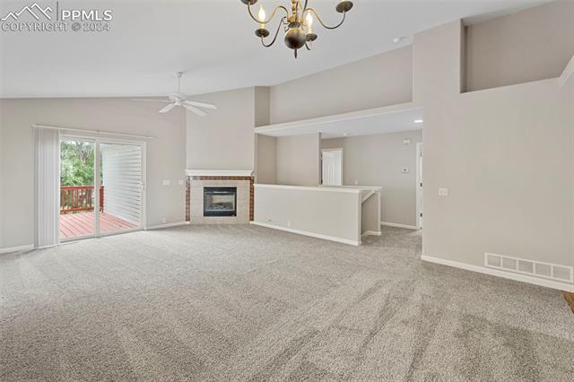 6725 Akron Road Colorado Springs, CO 80923 - Photo 12 of 50 Unfurnished living room featuring ceiling fan with notable chandelier, a tiled fireplace, carpet floors, and high vaulted ceiling