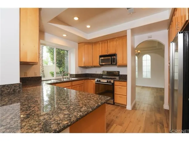 a kitchen with stainless steel appliances granite countertop a refrigerator a stove a sink dishwasher and a microwave with wooden floor