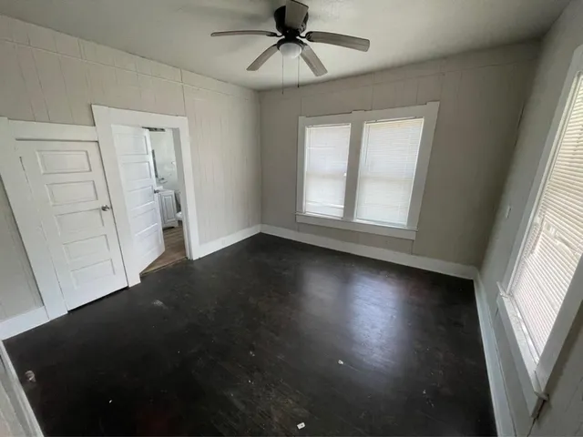 an empty room with wooden floor fan and windows
