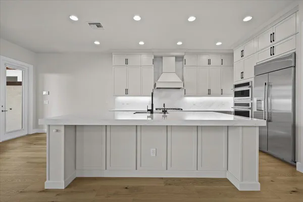 a large white kitchen with a lot of counter space and wooden floor