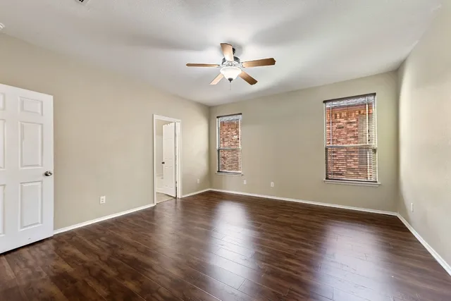 an empty room with wooden floor chandelier fan and windows