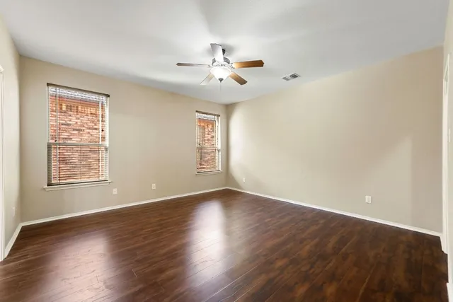 an empty room with wooden floor chandelier fan and windows