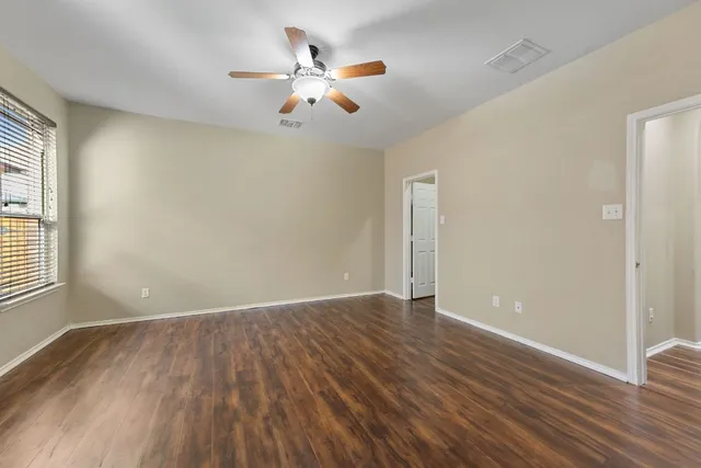 an empty room with wooden floor chandelier fan and windows