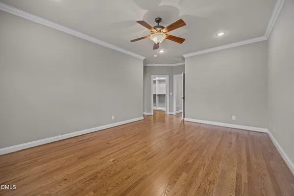 a view of an empty room with wooden floor and a ceiling fan