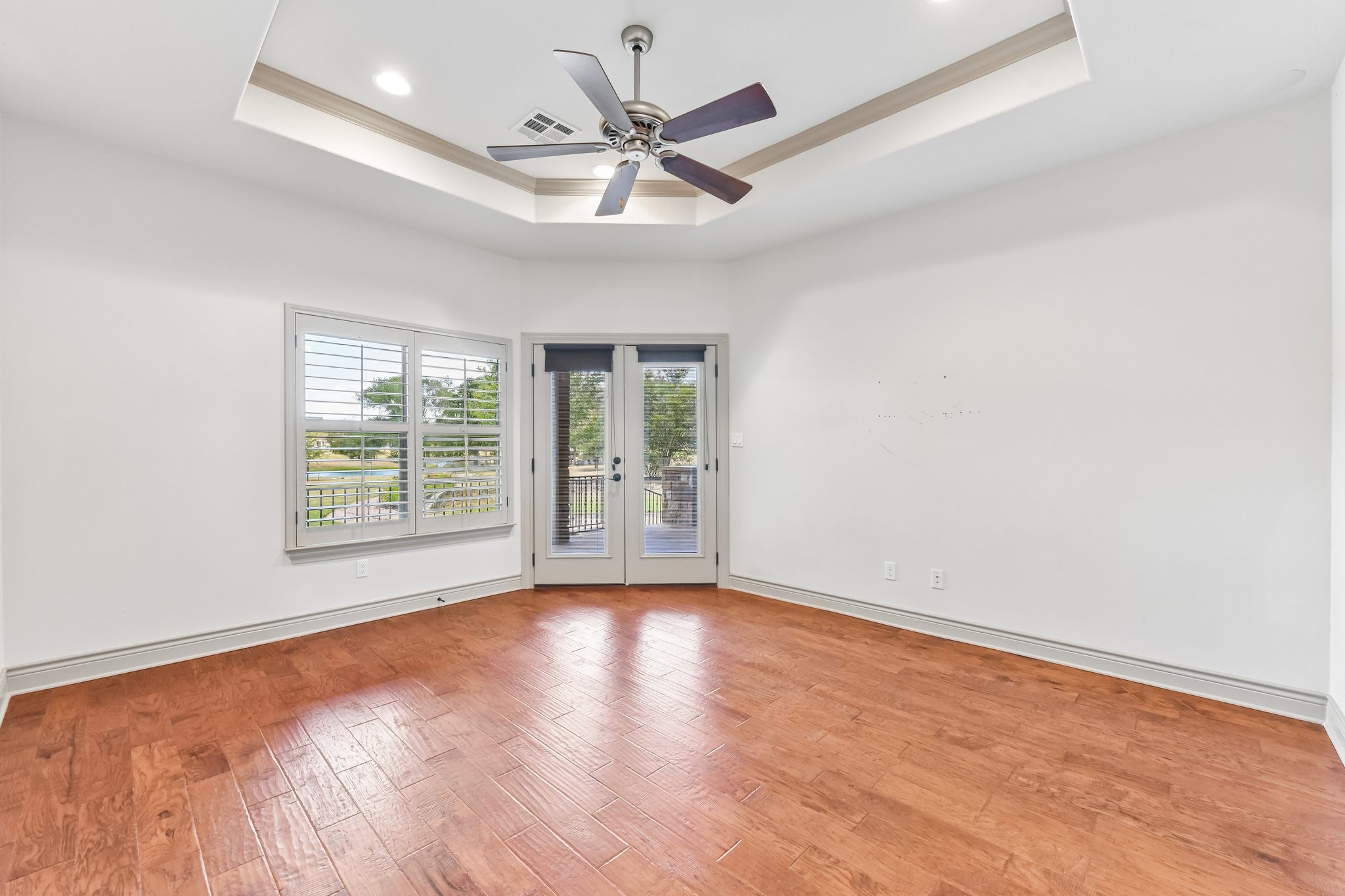 163 Powder Horn Road Bastrop, TX 78602 - Photo 23 of 34 Rich hardwood flooring complements the tray ceiling and glass doors leading outside.