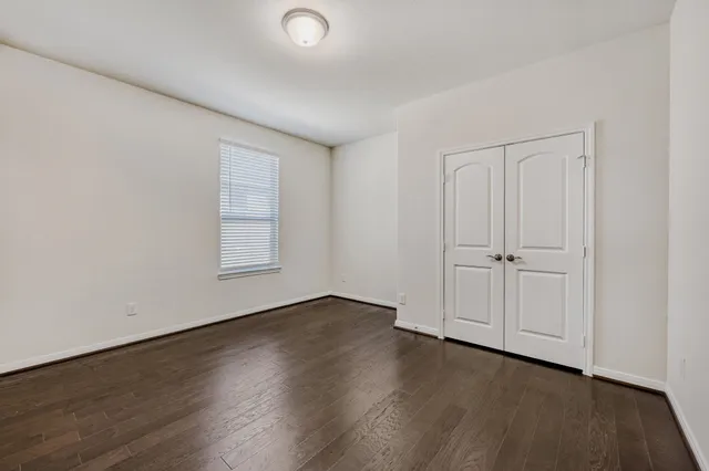 an empty room with wooden floor closet and windows