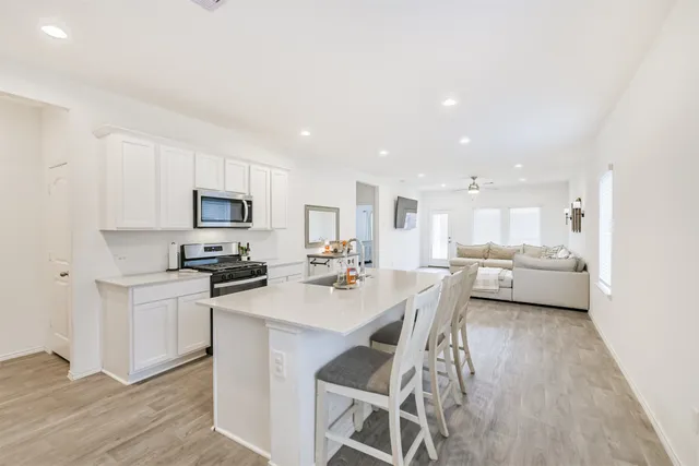 a kitchen with stainless steel appliances a stove a sink a refrigerator white cabinets and couches with wooden floor