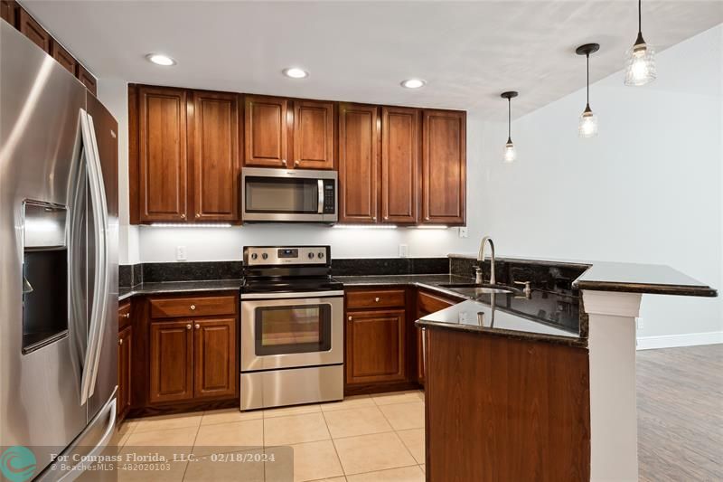 a kitchen with stainless steel appliances granite countertop wooden cabinets a stove a sink and a refrigerator