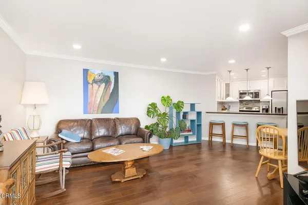 a living room with furniture and a kitchen view with wooden floor