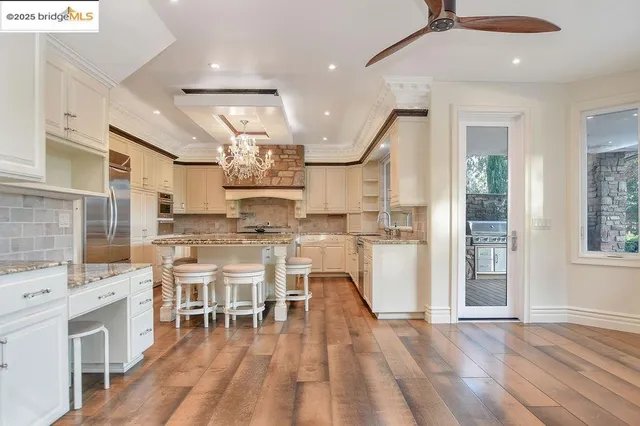 an open kitchen with granite countertop a stove a sink and white cabinets with wooden floor
