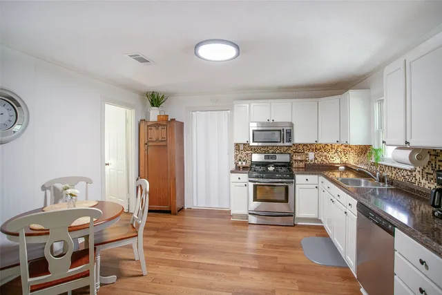 a kitchen with stainless steel appliances granite countertop a stove top oven a sink dishwasher and a refrigerator with wooden floor