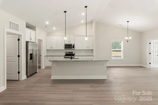 a view of a kitchen with stainless steel appliances kitchen island granite countertop a refrigerator a stove a kitchen island with wooden floor