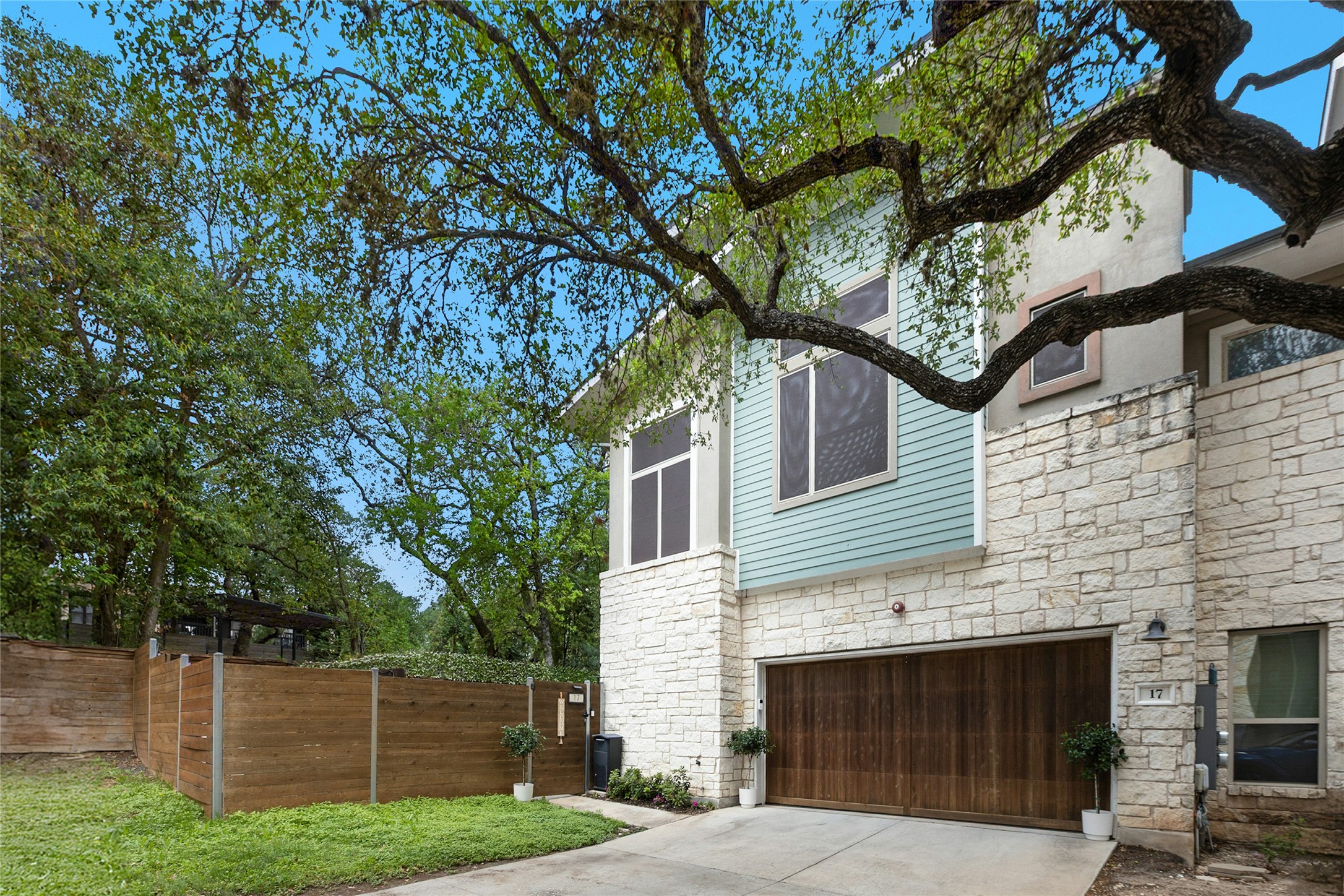 404 West Alpine Road, Unit 17 Austin, TX 78704 - Photo 2 of 35 Contemporary exterior with a wood-finish garage door, stone facade, light blue siding, and mature trees